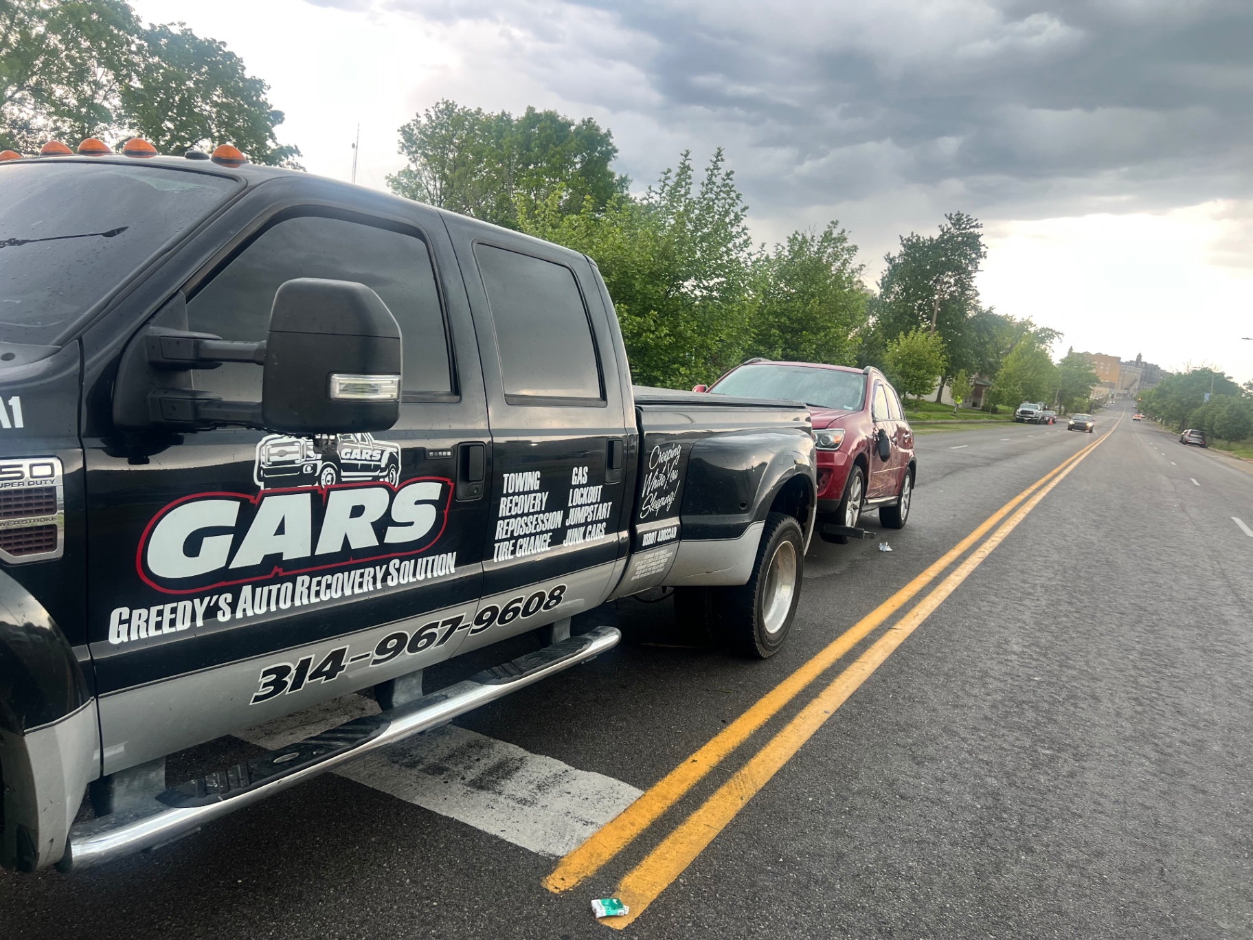 GARS tow truck on a St. Louis roadway at dusk with a red SUV in tow